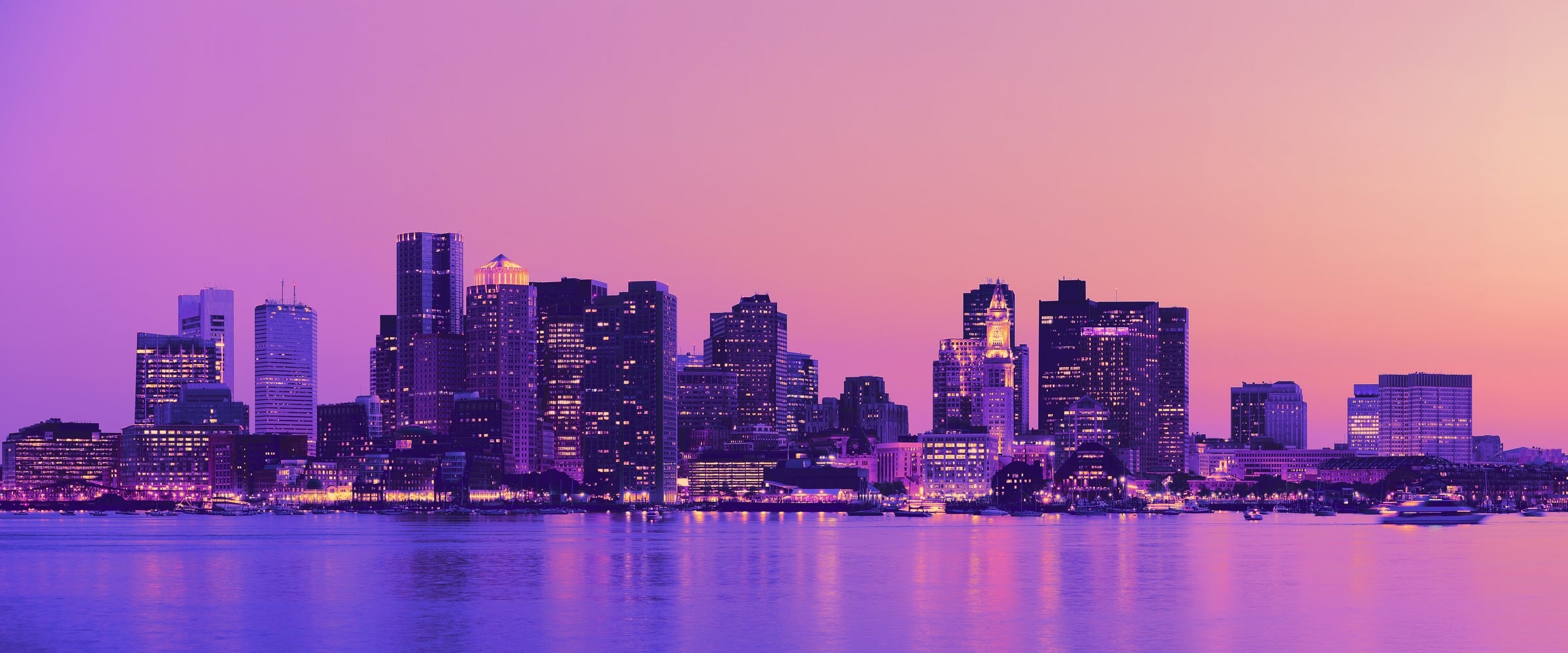 Boston skyline at sunset reflected across the harbor